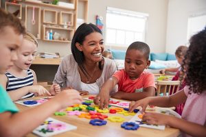 Preschool teacher sitting at a table with her students, engaged in an activity.