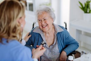 Nurse examining senior patient with stethoscope at her home.