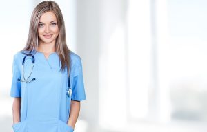 Female nurse wearing blue scrubs and standing in a medical setting.