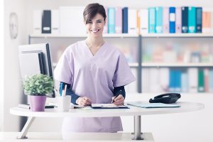 Female nurse wearing scrubs and sitting behind a desk.
