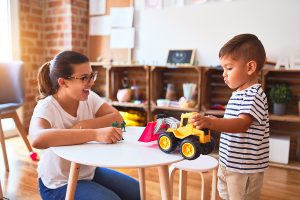 Preschool teacher working with a young student playing with a tractor.