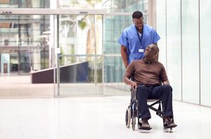 Male nursing assisting a male patient in a wheelchair. 